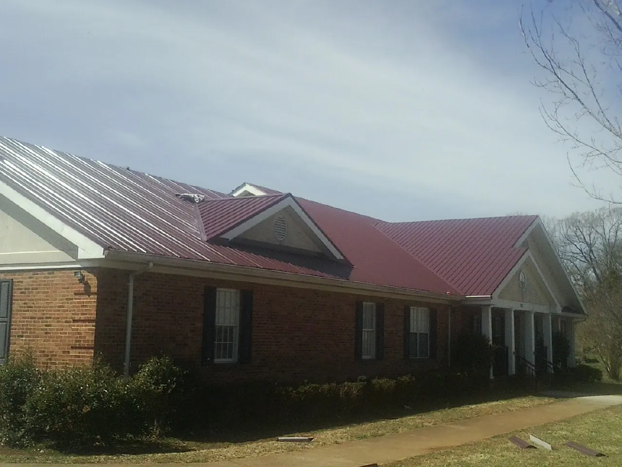 Red metal roof with gabled entries on a long brick building, from a Hail Damage Roof Repair job in Mattawan
