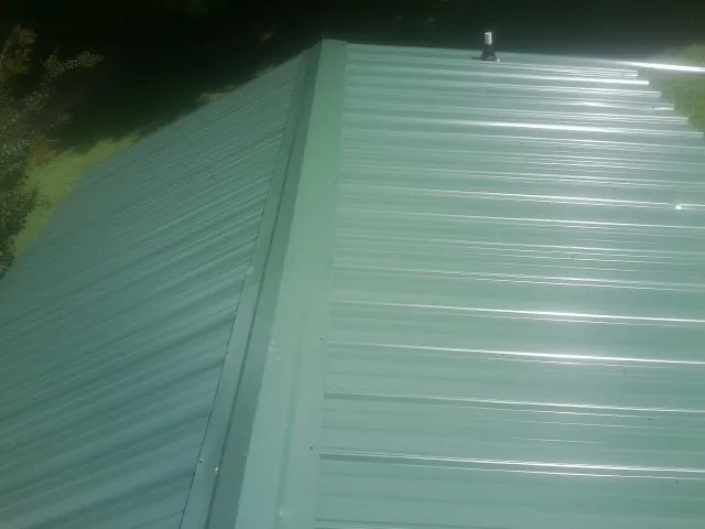 New green metal panels meeting at the ridge of a roof — Flat Roof Repair work by our crew in Mattawan