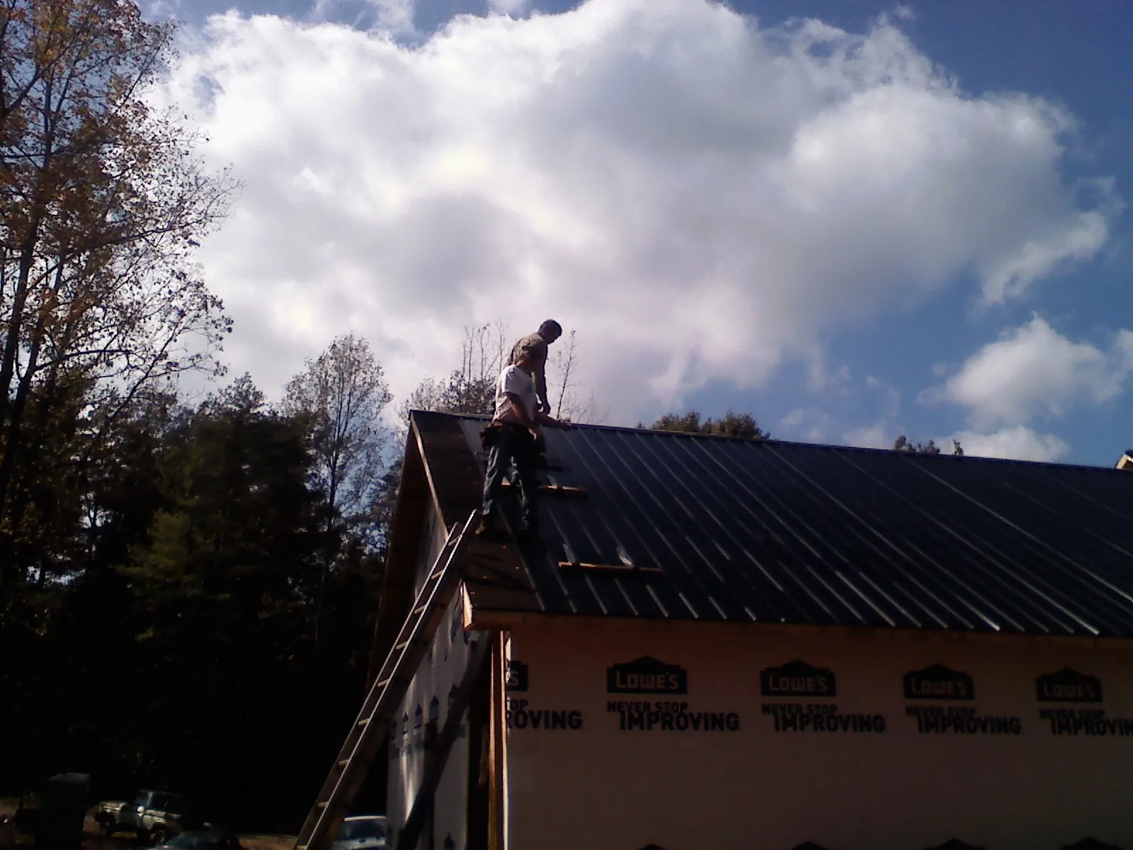 Roofer fastening dark metal panels high against a cloudy sky, from a Roof Inspection job in Mattawan