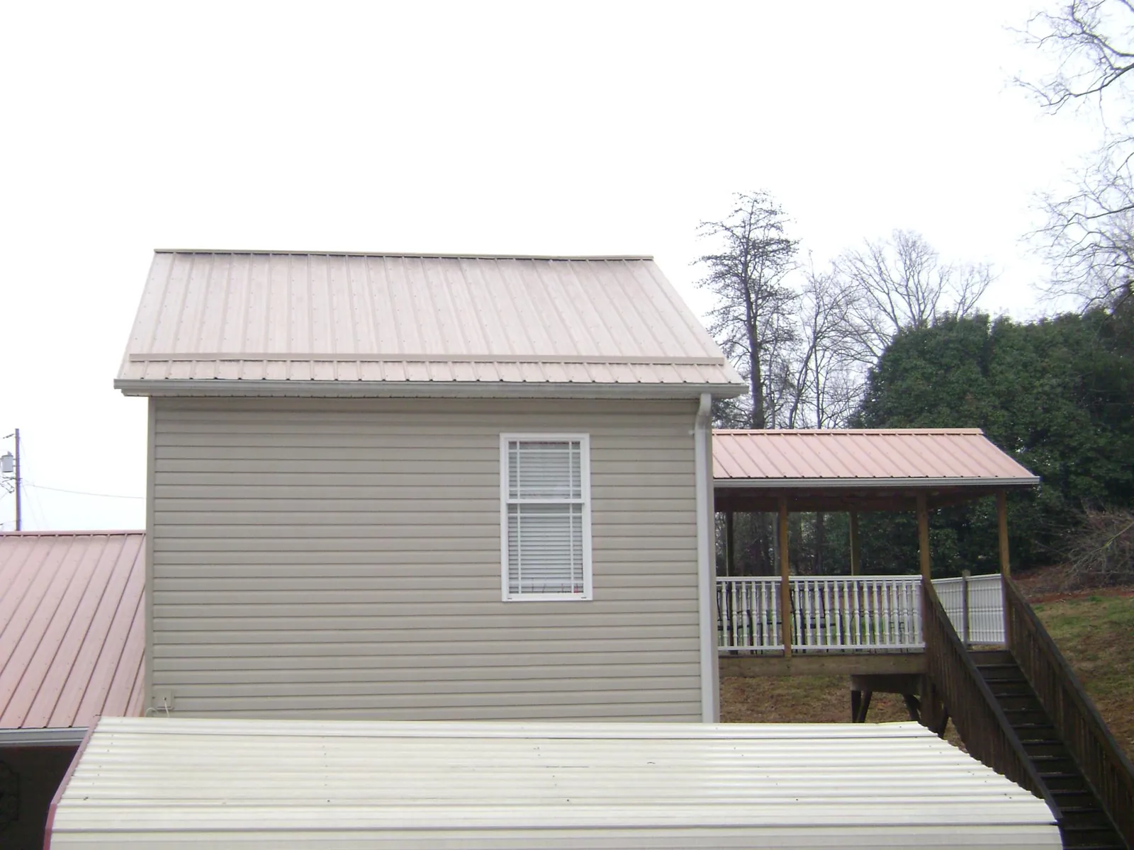 Tan metal roofs on a two story addition and attached porch, from a Roof Replacement job in Mattawan